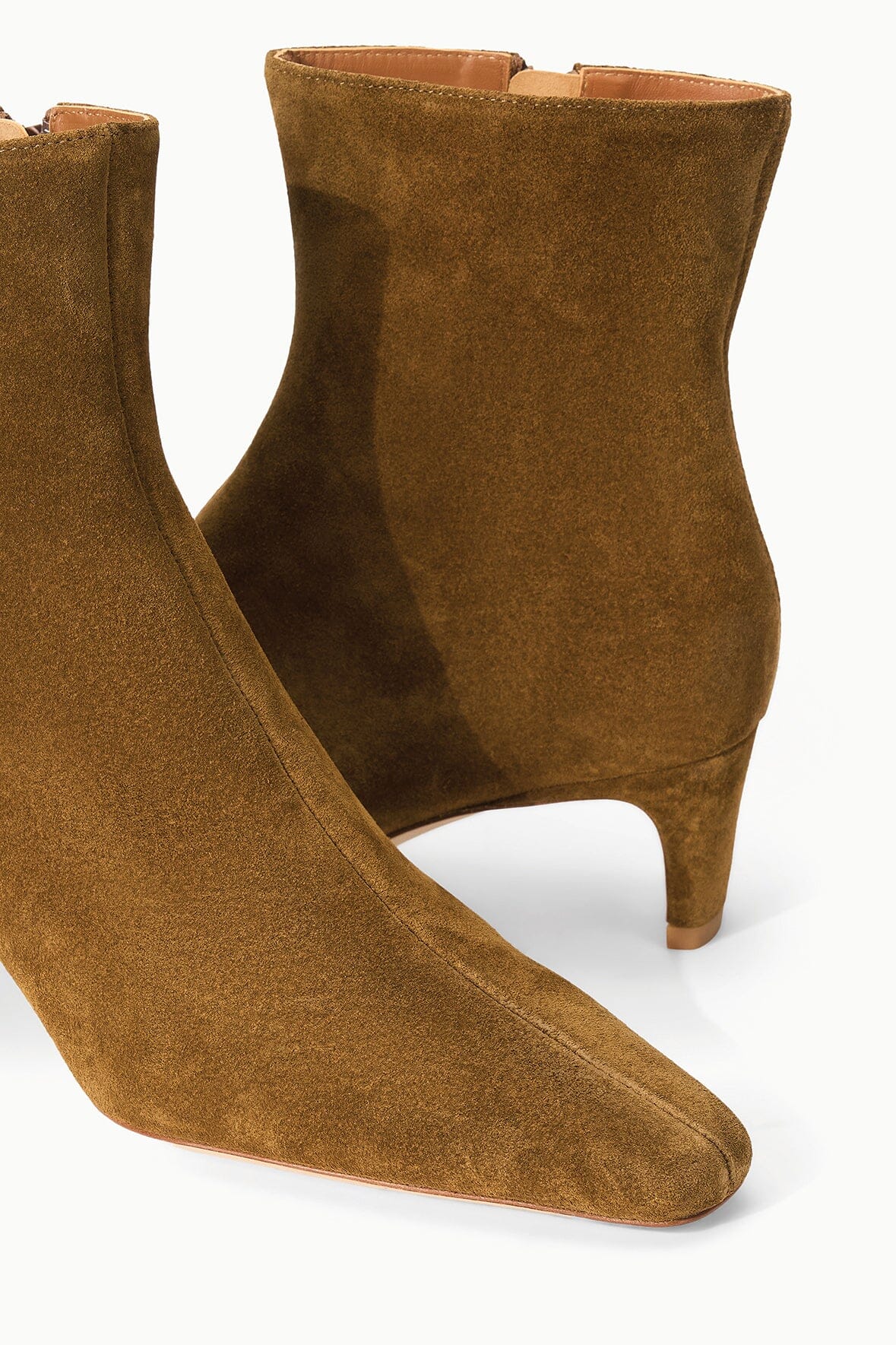 Two Staud Wally Suede Ankle Boots in brown, featuring pointed toes and low heels, displayed on a white background. This versatile style is perfect for adding an effortless touch of elegance to your everyday look.