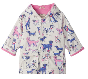 The Hatley Baby Girls’ and Girls’ Little Pups Rain Coat features a charming print of blue, pink, and purple cartoon dogs on a white background, a soft terry towelling lining, and two front pockets.