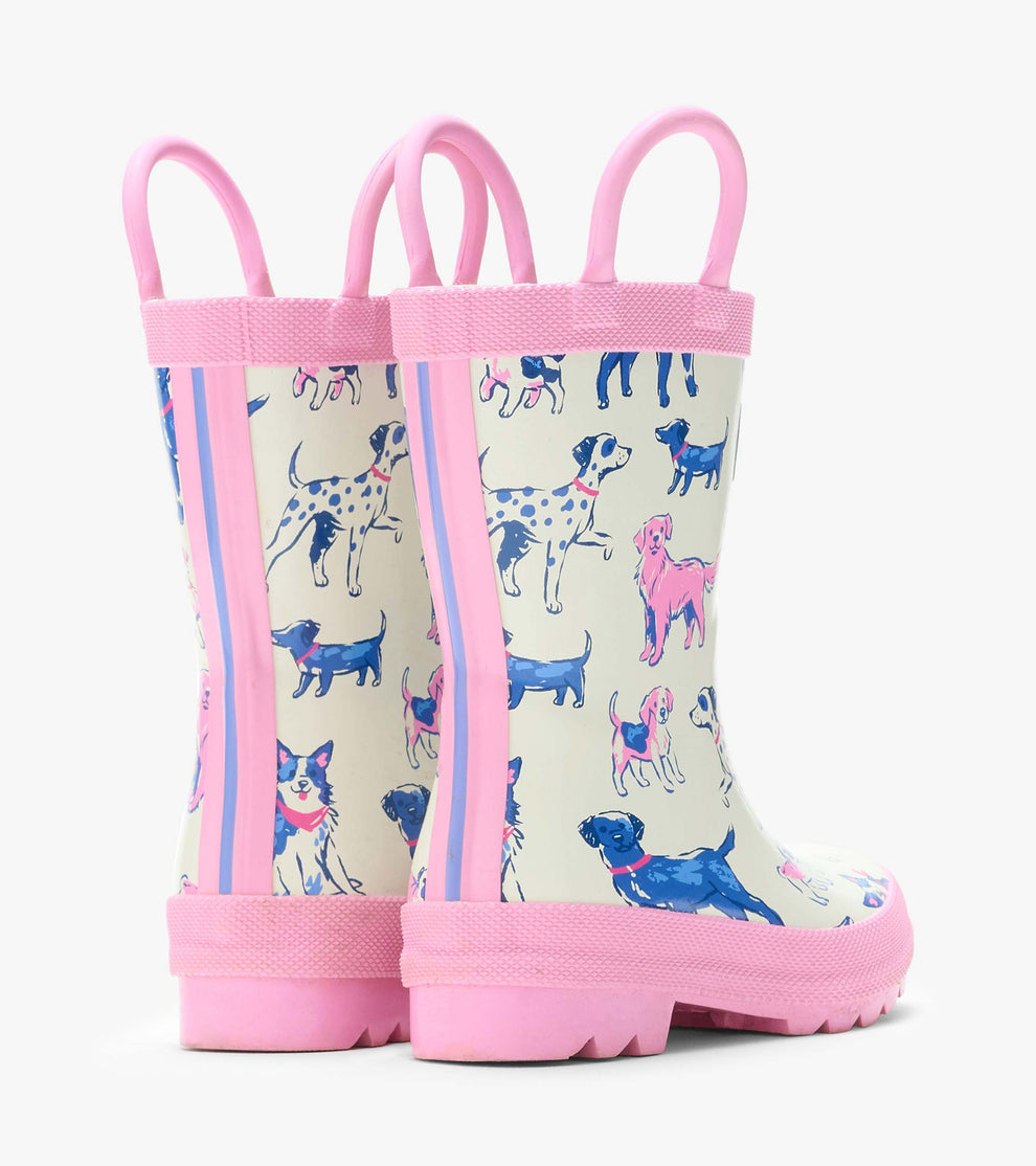 The Girls’ Little Pups Rain Boots by Hatley feature pink soles and trim, a slip-resistant design, and an illustrated pups print in shades of blue, pink, and purple on a white background. These adorable toddler boots are shown from the back and side.