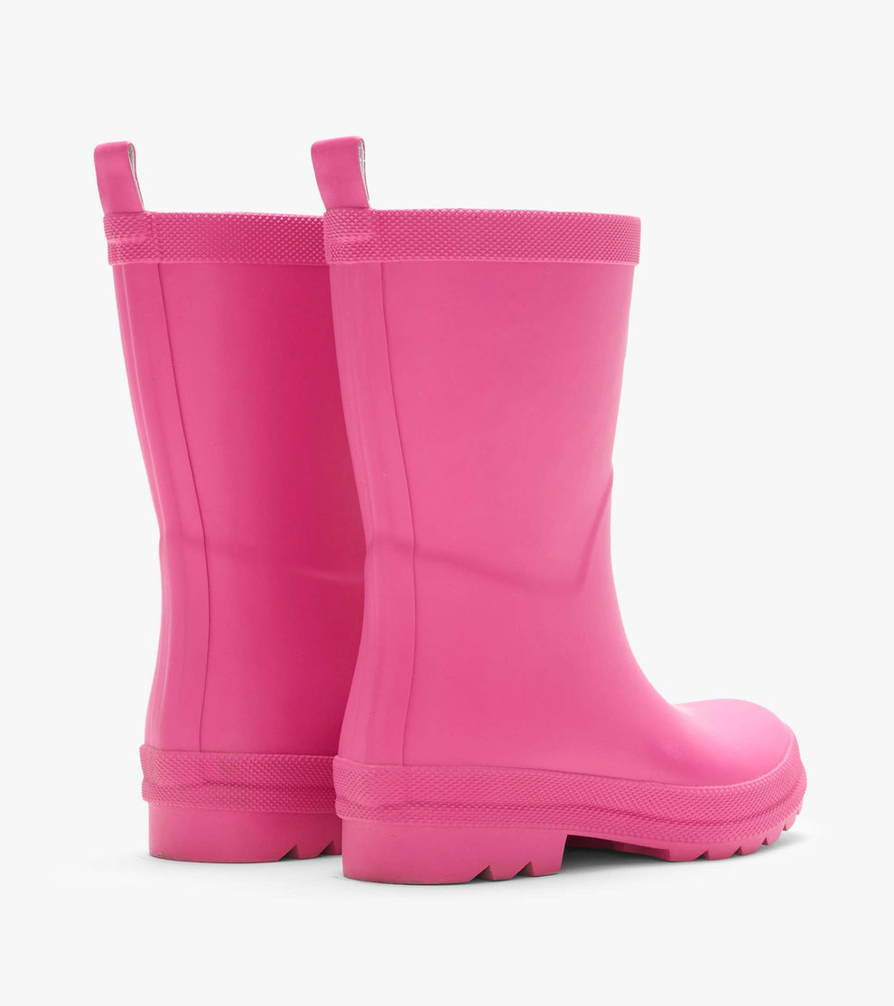 A pair of Hatley Girls’ Pink Yarrow Matte Rain Boots, featuring textured, slip-resistant soles and pull tabs, displayed from the back on a plain white background.