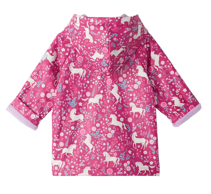 The Hatley Baby Girls’ and Girls’ Unicorn Forest Rain Coat is a pink rain jacket for children, featuring a hood and decorated with white unicorns and a floral pattern; the rolled-up sleeves reveal a light purple lining.