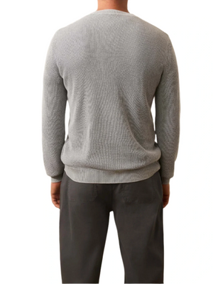 A person stands with their back to the camera, wearing the Faherty Sunwashed Crewneck Sweater in light gray textured cotton yarn and dark gray pants against a white background.