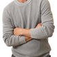 A bearded man stands with arms crossed against a white background, wearing the Faherty Sunwashed Crewneck Sweater in light gray cotton yarn and dark pants.