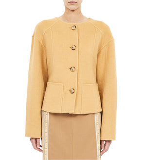 A person wearing the Ulla Johnson Elsie Wool Coat in camel, featuring buttons, long sleeves, and front pockets, paired with a beige skirt.