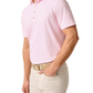 A man wearing the Johnnie-O Flock Yeah Performance Mesh Polo in light pink, paired with beige pants and a woven beige belt, stands with one hand in his pocket.