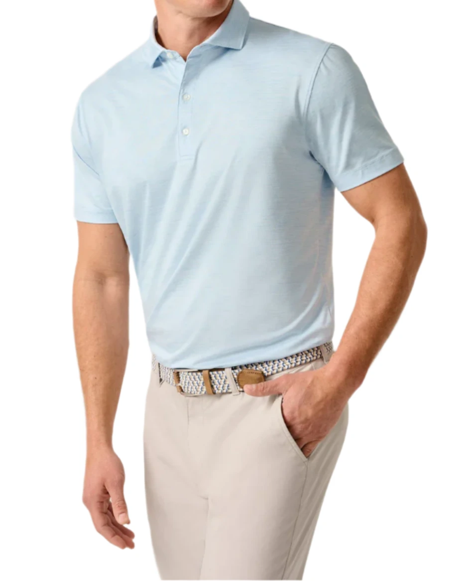 A man wearing the Johnnie-O Huronn Featherweight Performance Polo with UPF 50 sun protection, beige pants, and a patterned belt stands with one hand in his pocket against a white background.