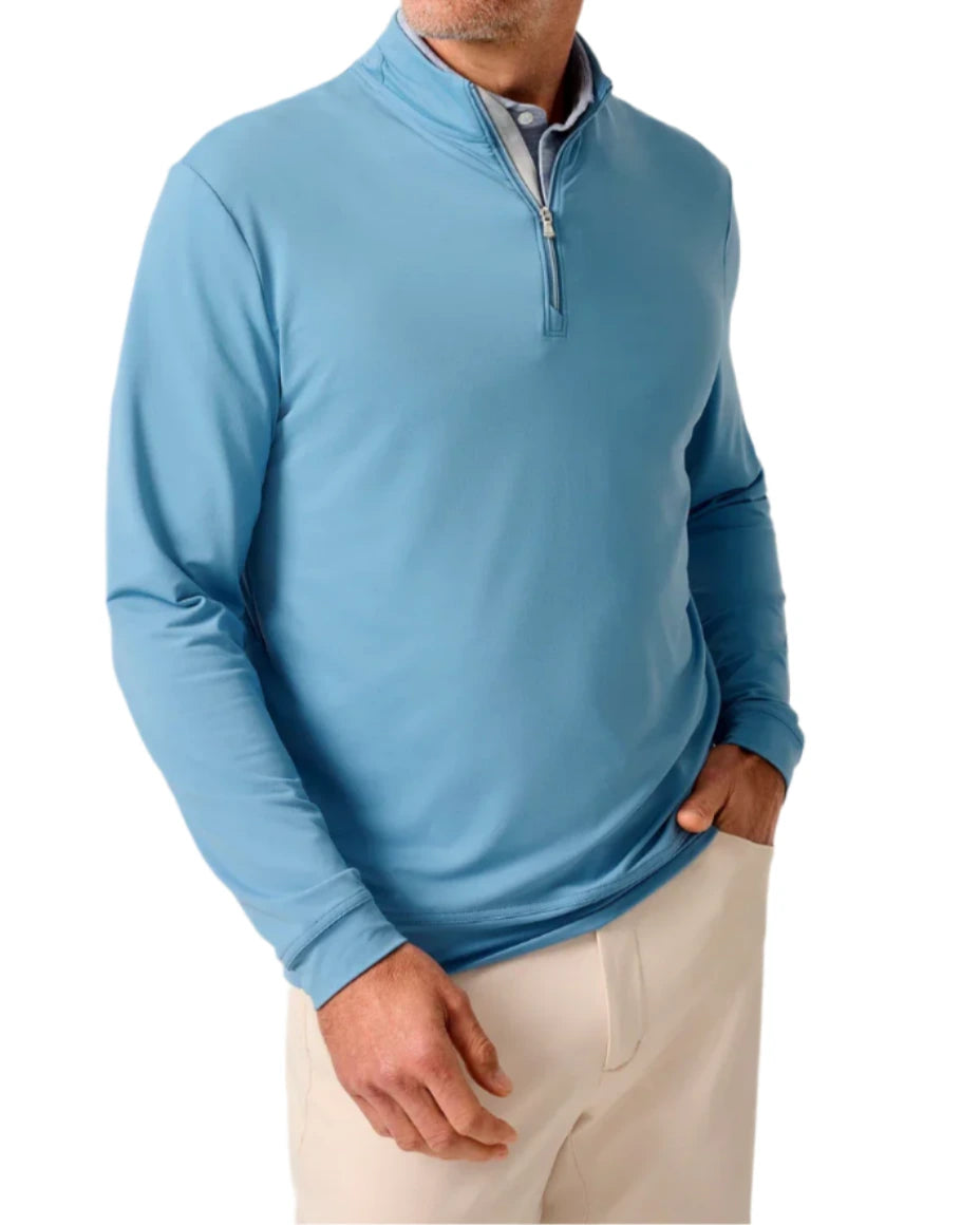 A man wearing a light blue Johnnie-O Motion Performance 1/4 Zip and beige pants, with one hand in his pocket.