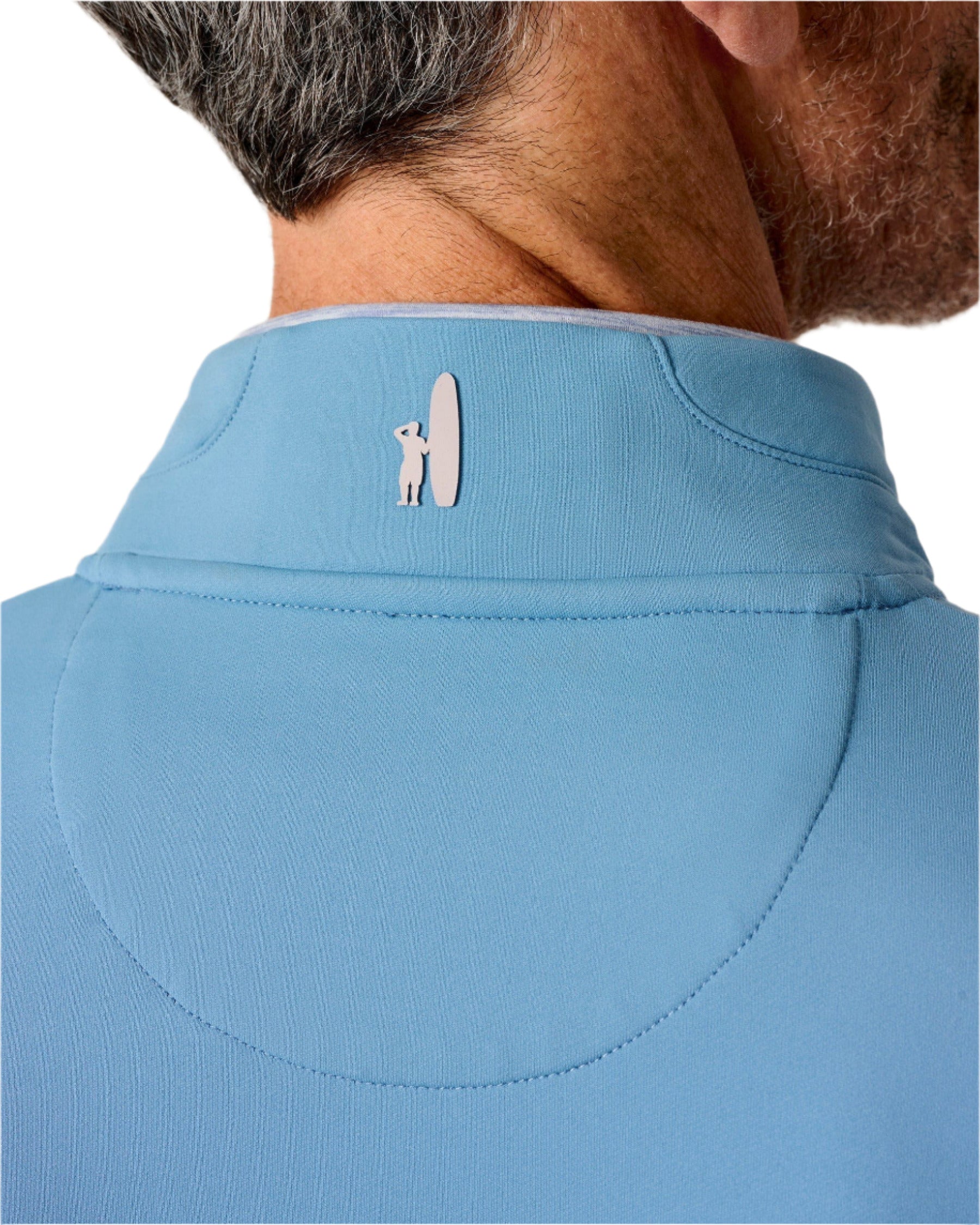 Close-up of the back of a man's neck and head, wearing a light blue Johnnie-O Motion Performance 1/4 Zip with a small white dog and surfboard logo on the collar.