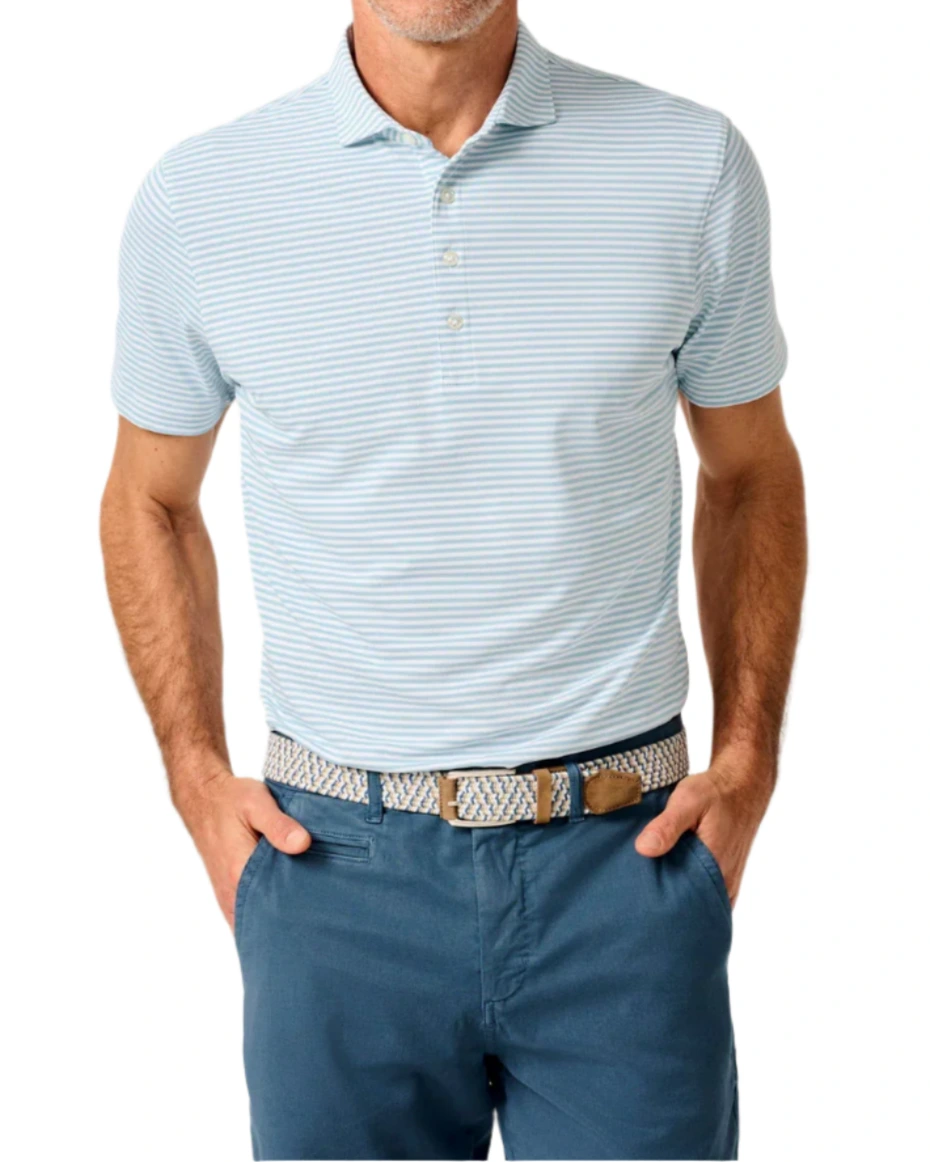 A man in the Johnnie-O Stetson Stripe Performance Mesh Polo—light blue and white stripes—wears blue pants and a woven belt with hands in his pockets, perfect for modern golf style.