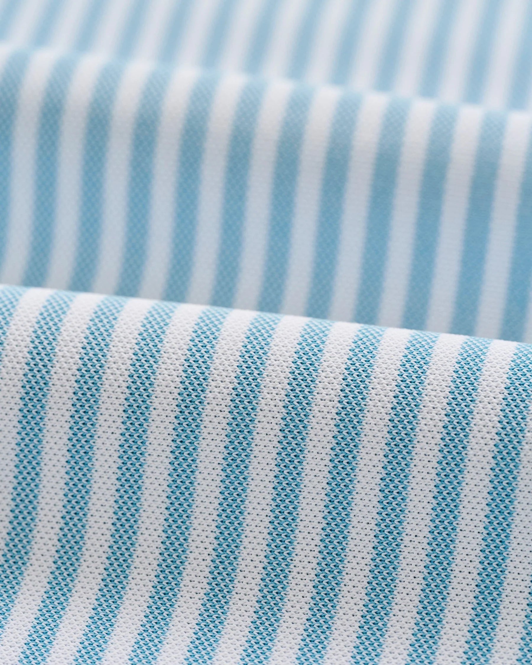 Close-up of light blue and white vertical stripes on the textured fabric of the Johnnie-O Stetson Stripe Performance Mesh Polo, shown in folds.
