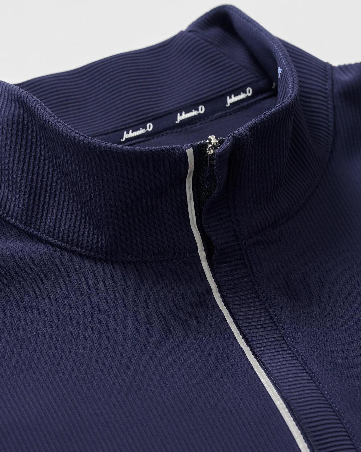Close-up of the Johnnie-O Hoppin QZ Pullover, a navy blue ribbed performance 1/4-zip athletic jacket with a stand-up collar and zipper, featuring a small white stripe alongside the zipper.