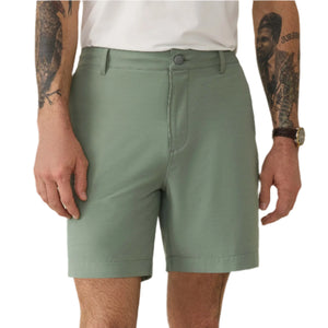 Dressed in Faherty's All Day Short 2.0, 7" in light green and a white shirt, the person stands with arms relaxed. Intricate tattoos adorn their left arm, while a watch graces their right wrist.