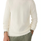 A person wearing the Faherty Sunwashed Crewneck Sweater in white and olive green pants, with hands in their pockets, shown from shoulders to thighs.