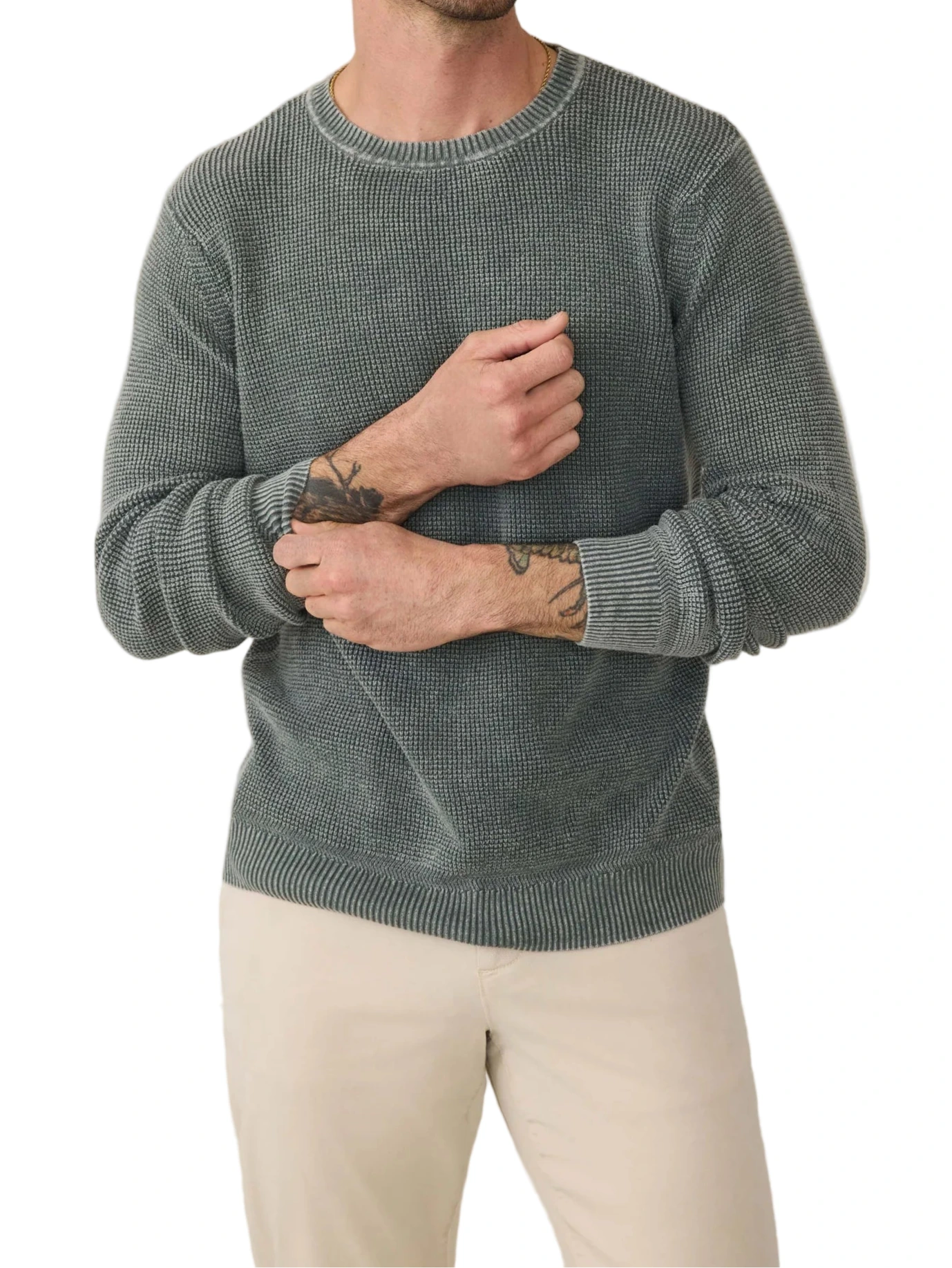 A person wearing the Faherty Sunwashed Crewneck Sweater in a textured waffle stitch with gray and light beige pants, showing visible forearm tattoos, stands against a white background.