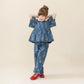 Young girl poses in a blue floral top and Pink Chicken Girls’ Theodore Pant with an elastic waist, paired with red shoes, against a plain beige background.