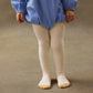 A young child stands on a neutral floor, wearing a blue long-sleeve dress and Louise Misha Baby Girls' and Girls' Chukata Tights in cream-colored soft cotton jersey knit.
