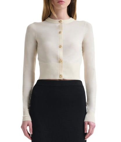 A woman wears the Altuzarra Arlette Sweater, a fitted, long-sleeve cream ribbed knit with two-tone metal buttons, paired with a high-waisted black skirt.
