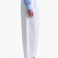 Person standing in profile wearing Altuzarra's white Dash Pant, a blue striped shirt with floral details, and beige flat shoes against a white background—an effortlessly chic look.