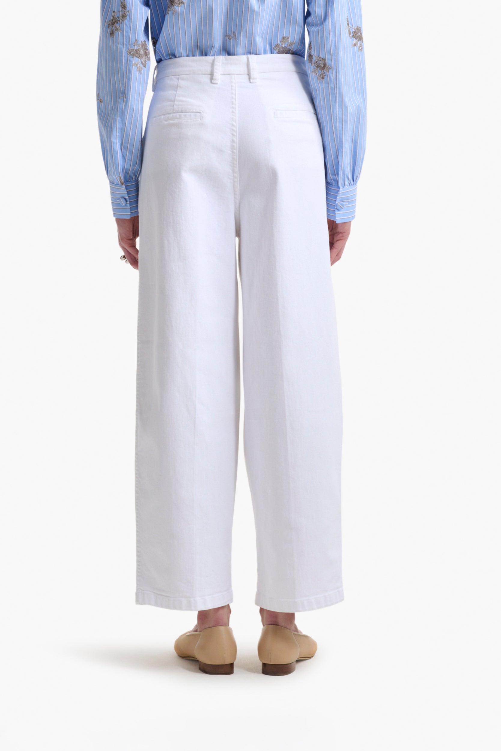 Person wearing the Altuzarra Dash Pant in white, paired with a light blue embroidered blouse and beige loafers, shown from the back against a plain background.