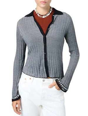 A person wears the Guest in Residence Fine Stripe Shirt, styled as a black and white button-up sweater over a brown top with white pants and beaded necklaces, standing against a white background.