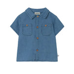 The Cozmo Baby Boys' Forest Chambray Shirt features blue denim, short sleeves, two chest pockets, brown buttons, and a collar, shown on a white background.