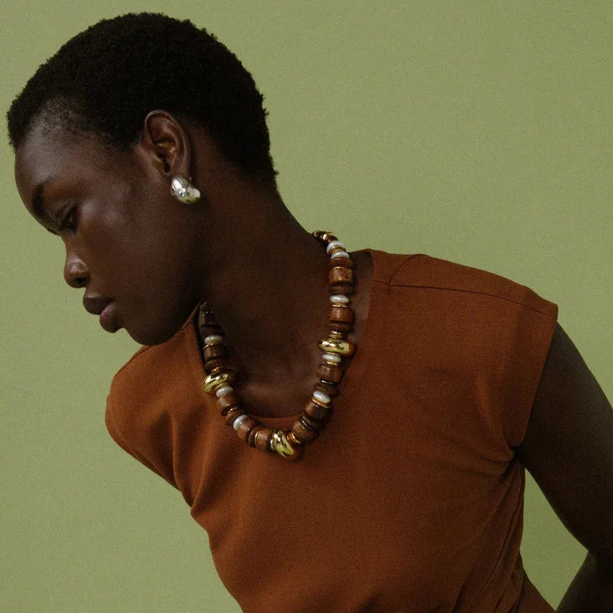 A person in a brown top adorned with Lizzie Fortunato Mini Arp Earrings looks away from the camera, against a green background.