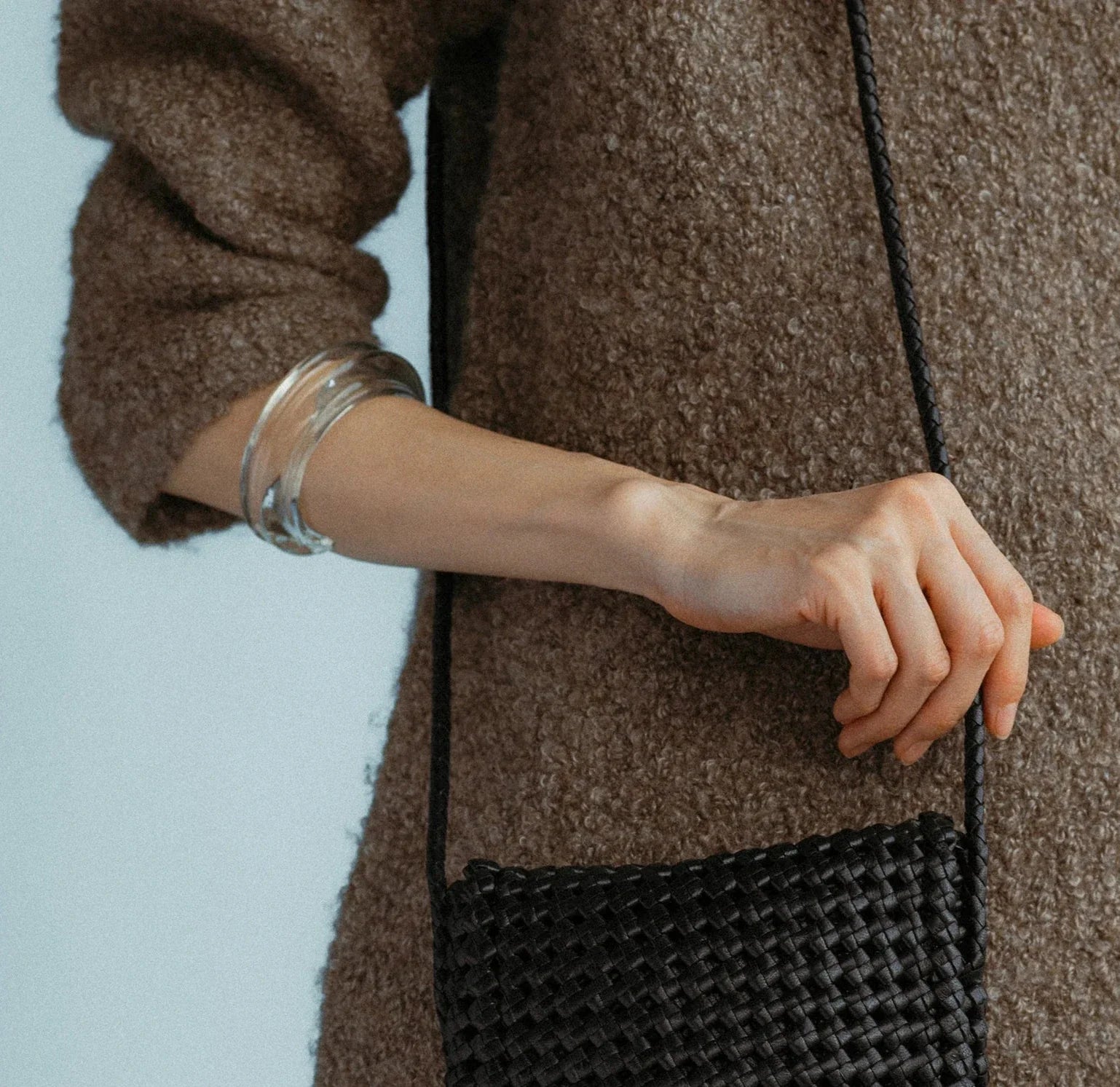 A person wearing a textured brown sweater holds a black woven bag. Their arm is adorned with the Lizzie Fortunato Onda Cuff, creating an elegant contrast against the ensemble.