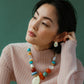 Woman wearing a ribbed, light pink turtleneck and colorful beaded necklace, looking to her left with her hand touching her Lizzie Fortunato Mini Arp Earrings by Lizzie Fortunato. Background is a solid green.