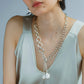 A person elegantly wears the Lizzie Fortunato Edith Lariat, paired with a silky light gray top.