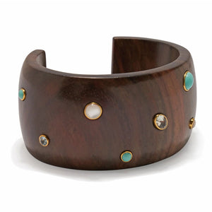 The Cara Cuff by Lizzie Fortunato is a wide, dark acacia wood bracelet adorned with inlaid turquoise gemstones and small round decorative accents.