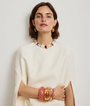 Woman in a white top wears colorful chunky jewelry—highlighted by the Lizzie Fortunato Ridge Marbled Cuff—alongside a pink resin beaded necklace, matching earrings, and several large bangles that pop against the plain backdrop.