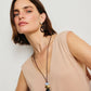 Woman with short brown hair models the Lizzie Fortunato Galina Earrings—gold and black statement pieces—paired with a sleeveless beige top and long beaded necklace, set against a plain light background.