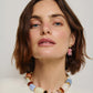A woman with short brown hair wears the Lizzie Fortunato Rosado Earrings—chunky, gold-plated brass with multicolored beads—shown against a plain background.