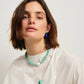 Woman with short brown hair wearing a white top and Lizzie Fortunato's Umbria Earrings, plus a turquoise beaded necklace and gold-plated brass pendant, against a plain light background.