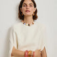 A woman in a white dress poses against a plain background, accessorized with chunky colorful jewelry including Lizzie Fortunato’s Satsuma Earrings, orange resin bracelets, and turquoise-colored stones.