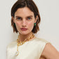 A woman with short brown hair wears a cream sleeveless top, gold pendant necklace, and Lizzie Fortunato Zellige Hoops—handcrafted green earrings—standing against a plain white background.