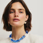 A woman with short brown hair wears a white top, a chunky blue and white beaded necklace, and one Lizzie Fortunato Pearl Pablo Earring (gold-plated sterling silver), looking at the camera against a plain background.