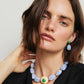 Woman with short brown hair wears a black top and the Lizzie Fortunato Andalusia Collar, a blue chalcedony necklace with a large central pendant, semiprecious details, and matching green and blue earrings.