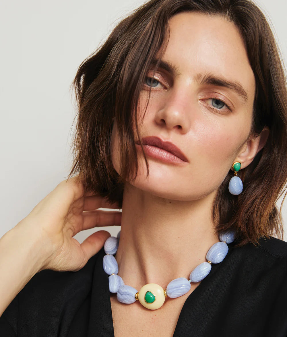 Woman with short brown hair wears a black top and the Lizzie Fortunato Andalusia Collar, a blue chalcedony necklace with a large central pendant, semiprecious details, and matching green and blue earrings.