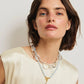 A woman with short brown hair in a cream sleeveless top and layered necklaces—including Lizzie Fortunato’s Pearl Isle Necklace—stands against a plain background.
