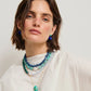 Woman with short brown hair wears the Lizzie Fortunato Cabana Necklace, a layered blue and green beaded piece, paired with a gold pendant necklace, blue earrings, and a white top, facing forward against a plain background.