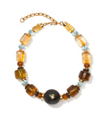 The Desert Mirage Collar by Lizzie Fortunato features gold, amber, blue, and black beads—including a bold central black bead, striking flame-worked glass accents, and an adjustable gold chain clasp.