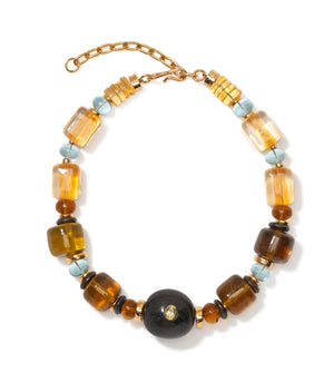 The Desert Mirage Collar by Lizzie Fortunato features gold, amber, blue, and black beads—including a bold central black bead, striking flame-worked glass accents, and an adjustable gold chain clasp.