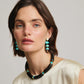 Woman with short brown hair wearing a cream blouse and Lizzie Fortunato’s Cathedral Collar necklace, styled with turquoise drop earrings, poses in front of a plain background.