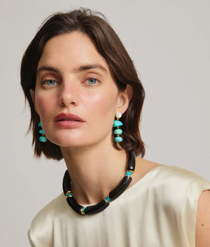 Woman with short brown hair wearing a cream blouse and Lizzie Fortunato’s Cathedral Collar necklace, styled with turquoise drop earrings, poses in front of a plain background.