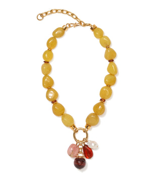 The Cordoba Charm Necklace by Lizzie Fortunato is a bold gold statement piece featuring large yellow beads and a central ring with five assorted gemstone pendants in red, pink, and white tones.
