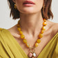 Woman wearing a yellow top, gold earrings, and the Lizzie Fortunato Cordoba Charm Necklace featuring statement beads with large pendants, shown from shoulders up.
