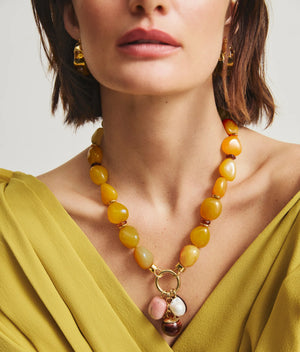 Woman wearing a yellow top, gold earrings, and the Lizzie Fortunato Cordoba Charm Necklace featuring statement beads with large pendants, shown from shoulders up.