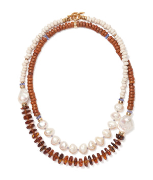 The Cabana Necklace by Lizzie Fortunato showcases two strands—one with white and brown beads, the other with pearls, amber discs, and blue accents—finished with a gold clasp. A statement piece to elevate any outfit.
