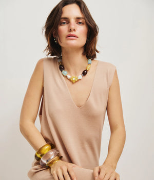 A woman with shoulder-length brown hair wears a sleeveless beige dress and the Lizzie Fortunato Mistflower Necklace, seated against a plain light background.